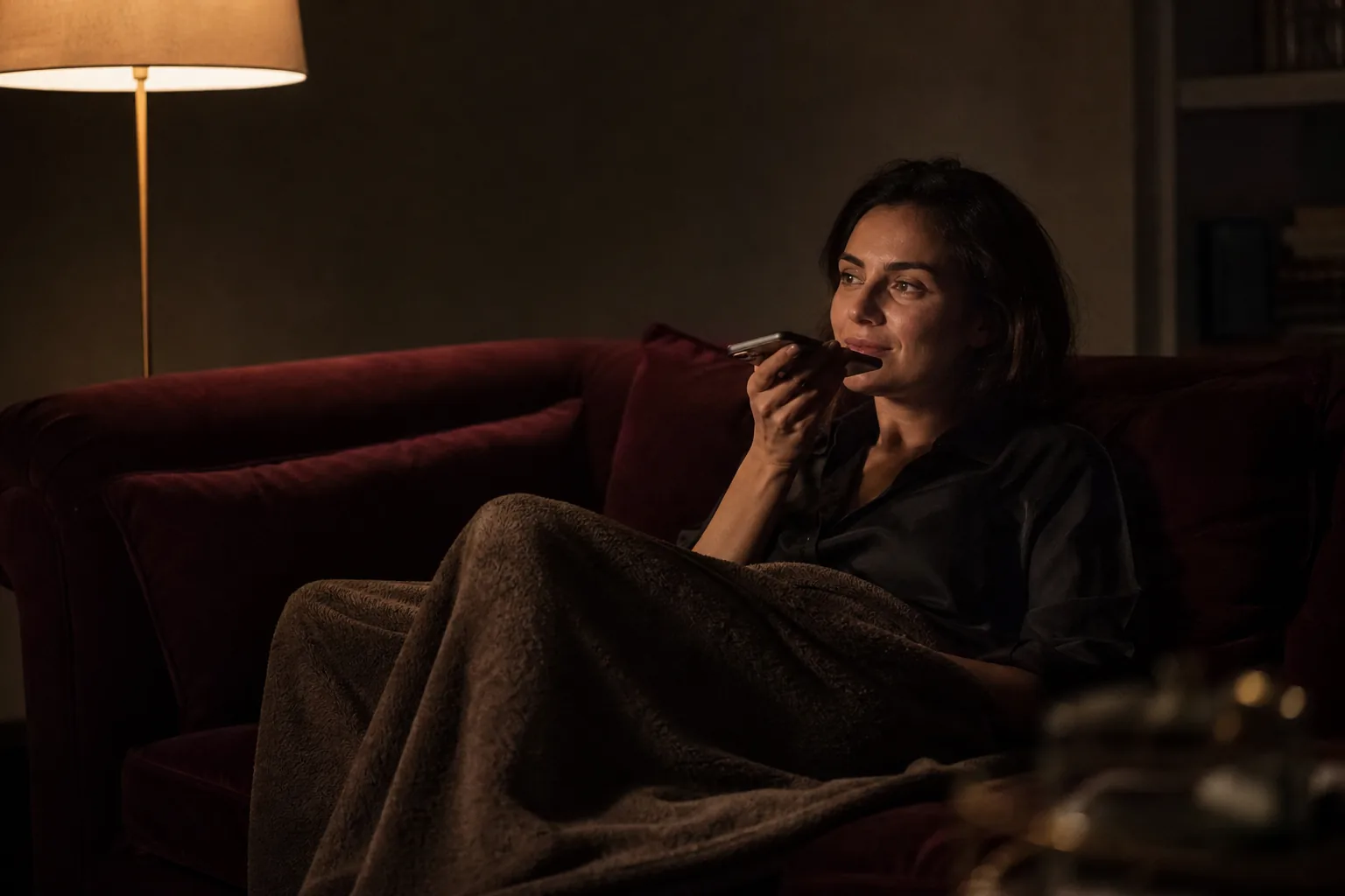 Creator recording a short voice note on her phone on a dark sofa