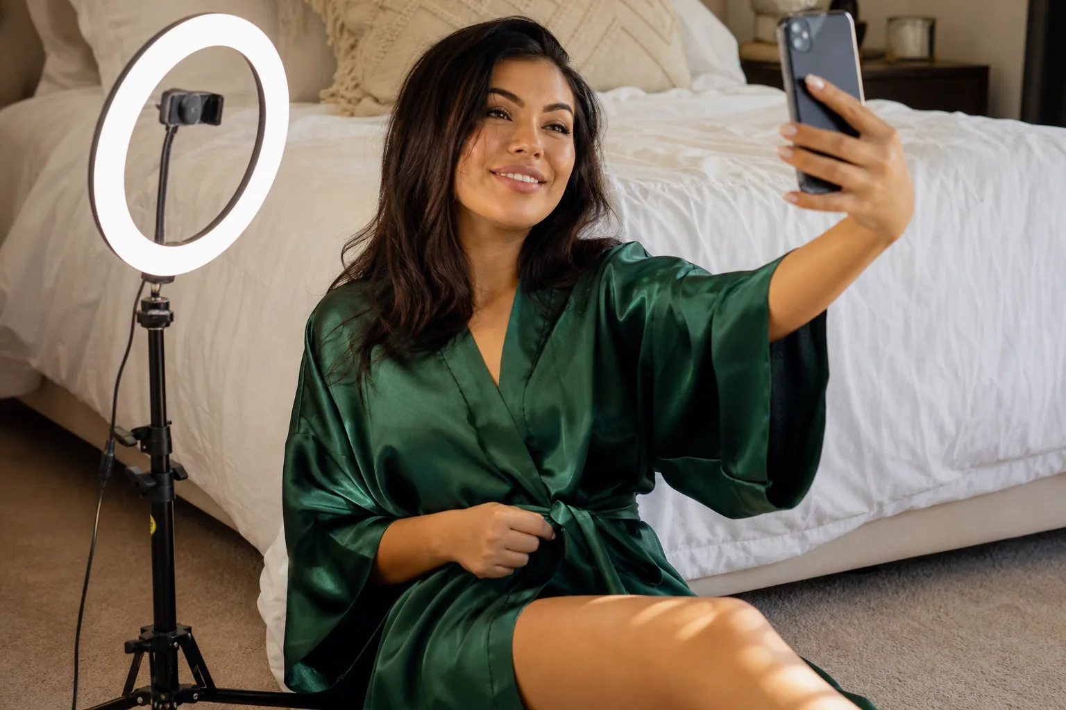 Creator in an emerald satin robe recording a short clip with her phone by a ring light